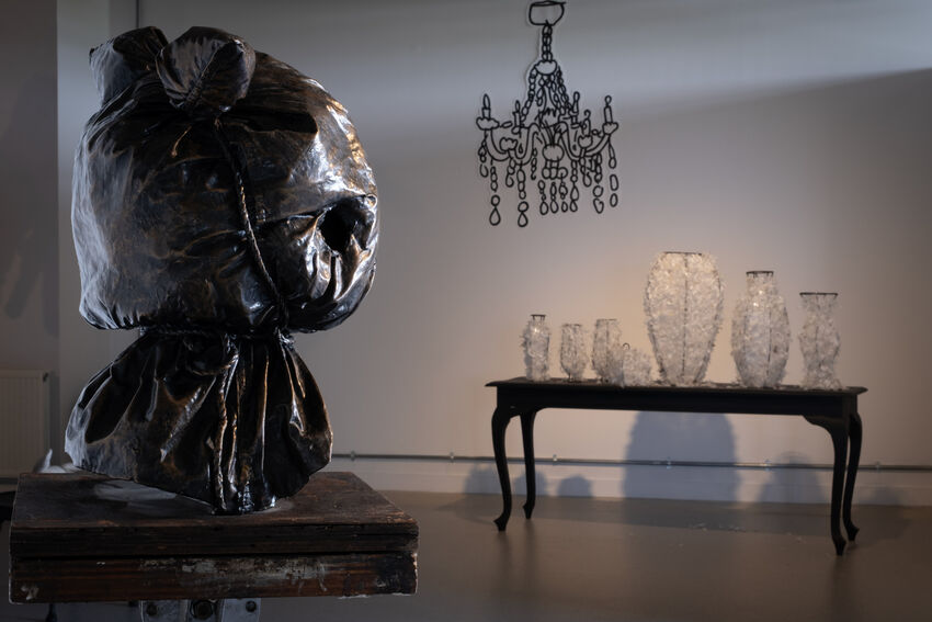 Art exhibtion within a dimly lit room featuring a chain chandelier and scultures on tables