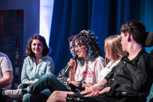 A panel of people, with one person in the middle speaking in to a microphone
