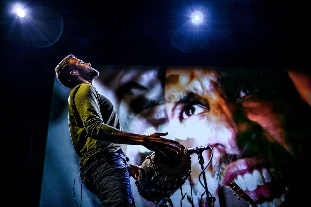 Aditya Prakash plays a double-headed drum, alarge projection of his face behind him