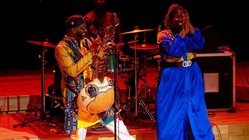 Seckou Keita holds the Kora and dances and claps with a member of his Homeland Band