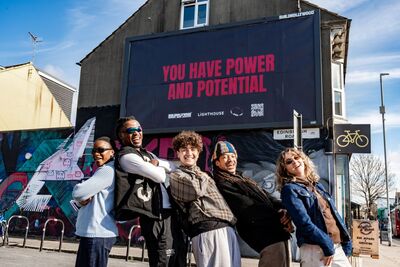 Some of Lighthouse's Future Creative Leaders stand in the street in front of a billboard that reads You hev power and potential