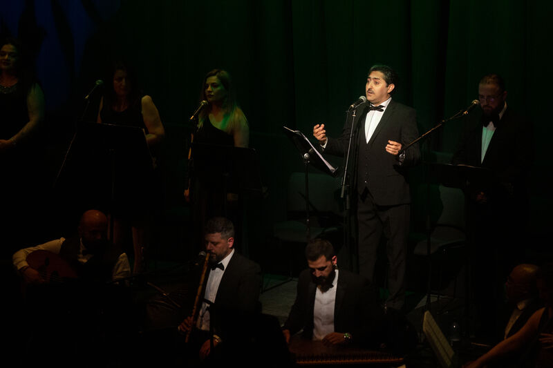Man in tuxedo in spotlight singing in to microphone
