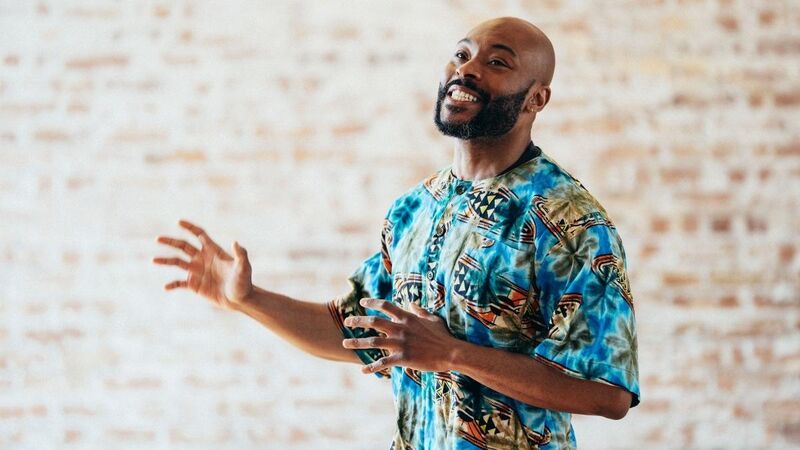 Arinze, a black man in a brightly patterned shirt, gestures with his hands