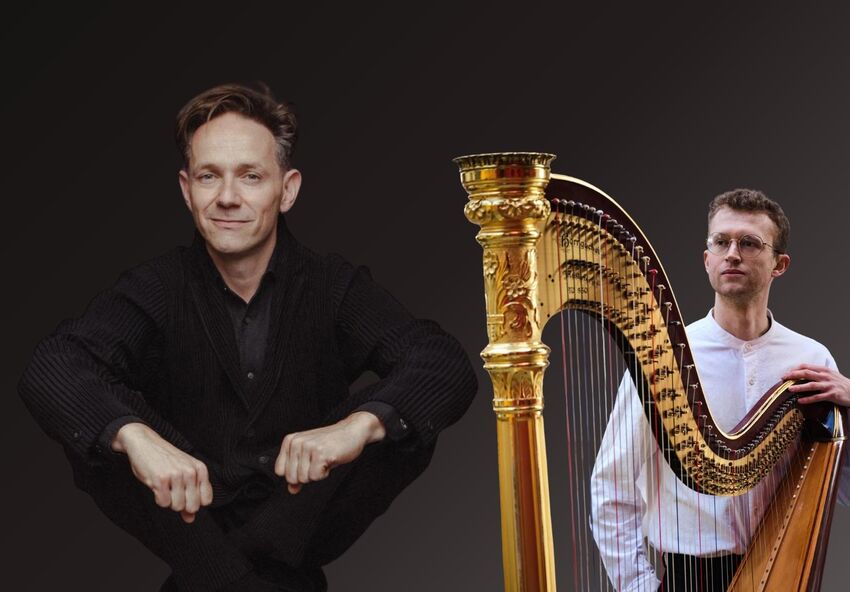 Two men pose against a dark background with a large golden harp between them; one man in black sits with his arms resting on his knees, while the other, wearing glasses and a light shirt, stands beside the harp holding it.