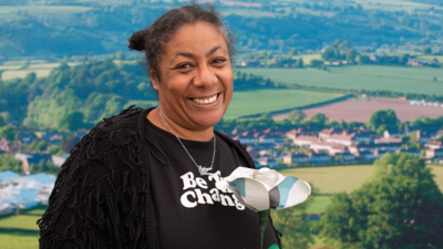 Patrice Lawrence smiling holding a paper rose with the country side in the background