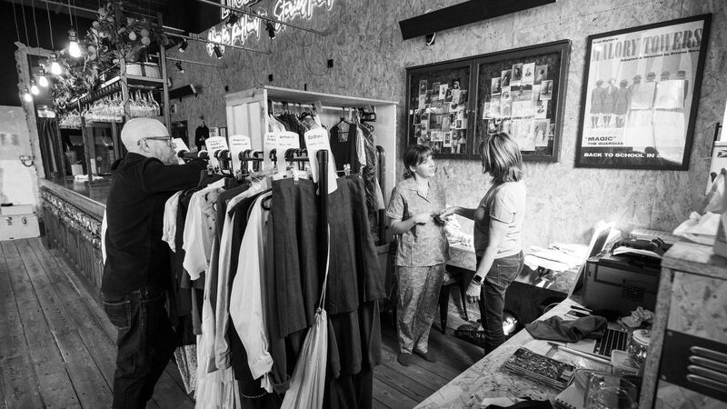 Two clothes racks full of costumes stand in front of two women having a conversation