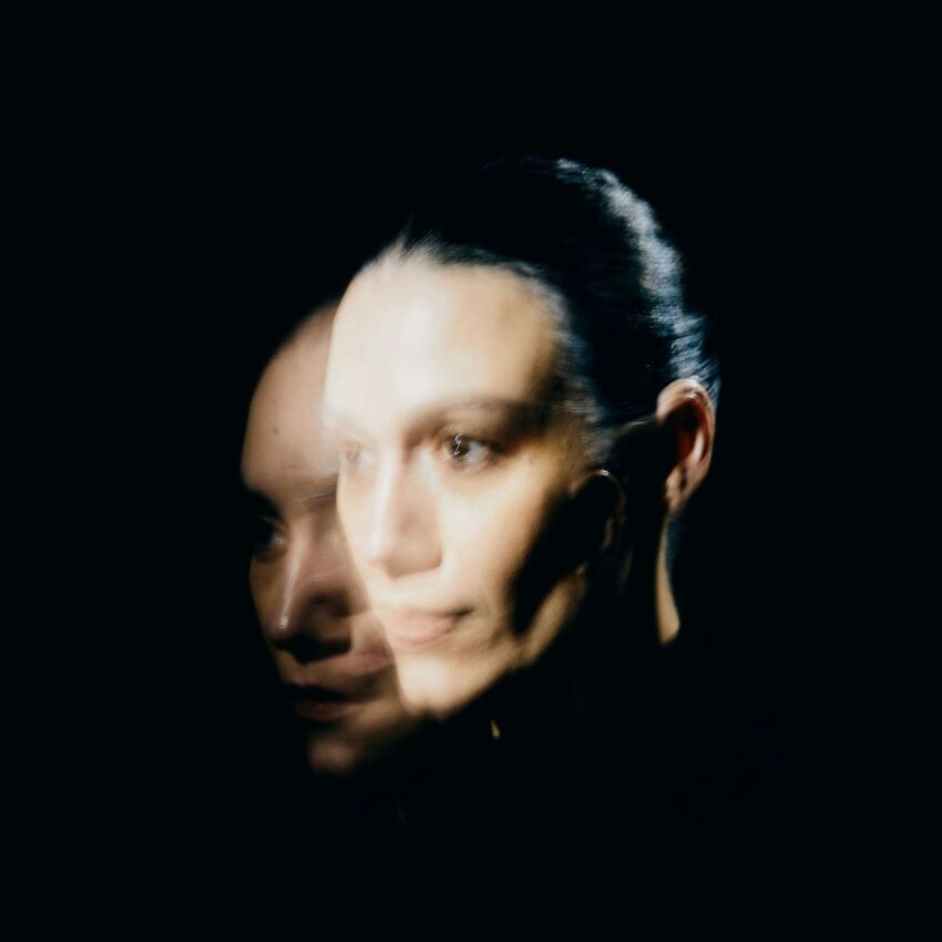 A dark shadowy portrait photo of Nadine Shah, two of her face overlayed