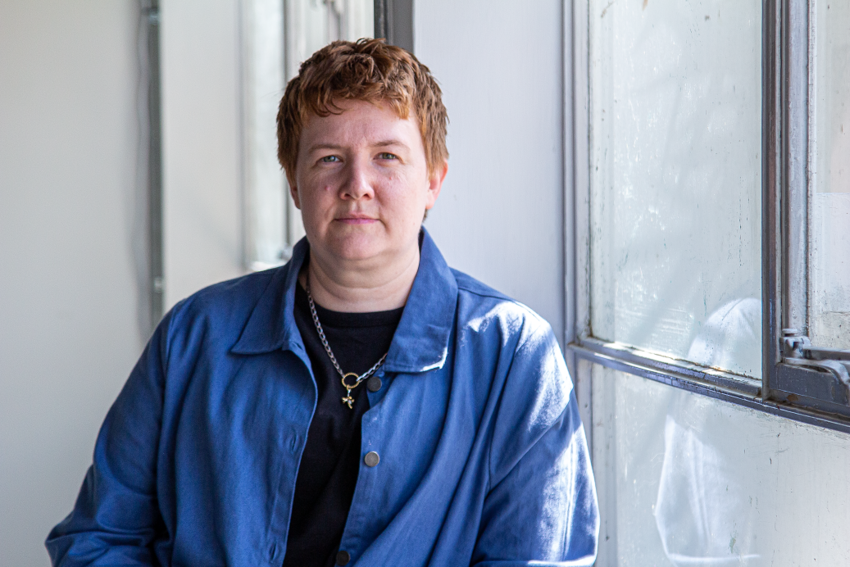 Elizabeth Lovatt, a white woman with short reddish hair, leans against a window
