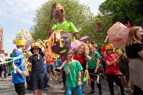 A group of children parade through the street with giant sculptures. They are all smiling and having a good time