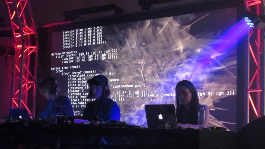 A row of three DJs using laptops in front of a screen with projections of live code