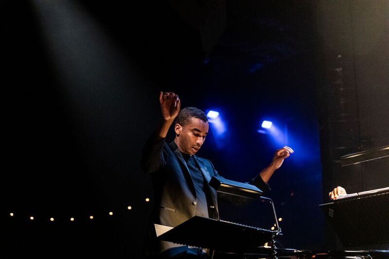 A band conductor has both arms raised and is looking at sheet music