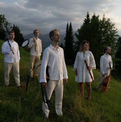 5 musicians holding early instruments on a green hillside wearing loose white clothing