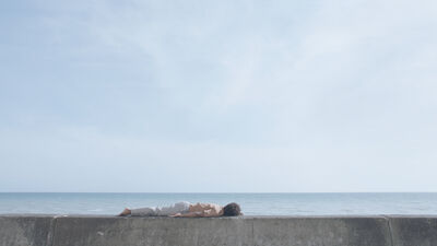 A man lies face down on a concrete, behind him only the sea and the sky