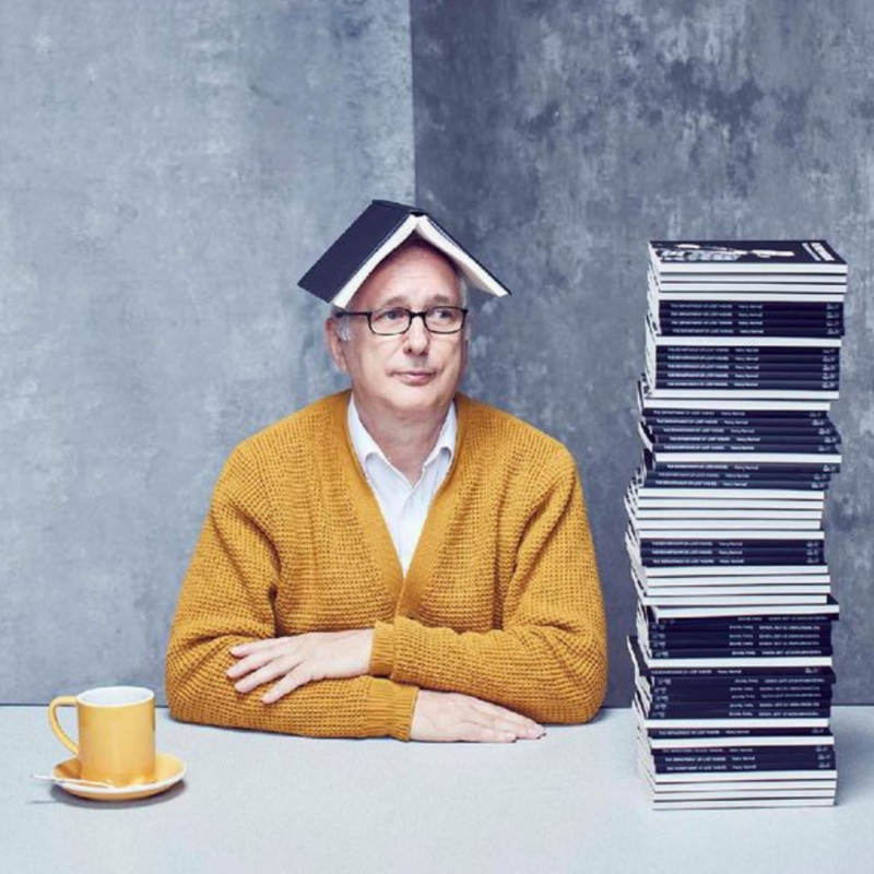 Henry Normal sat at a table with a book on his head next to a big stack of books