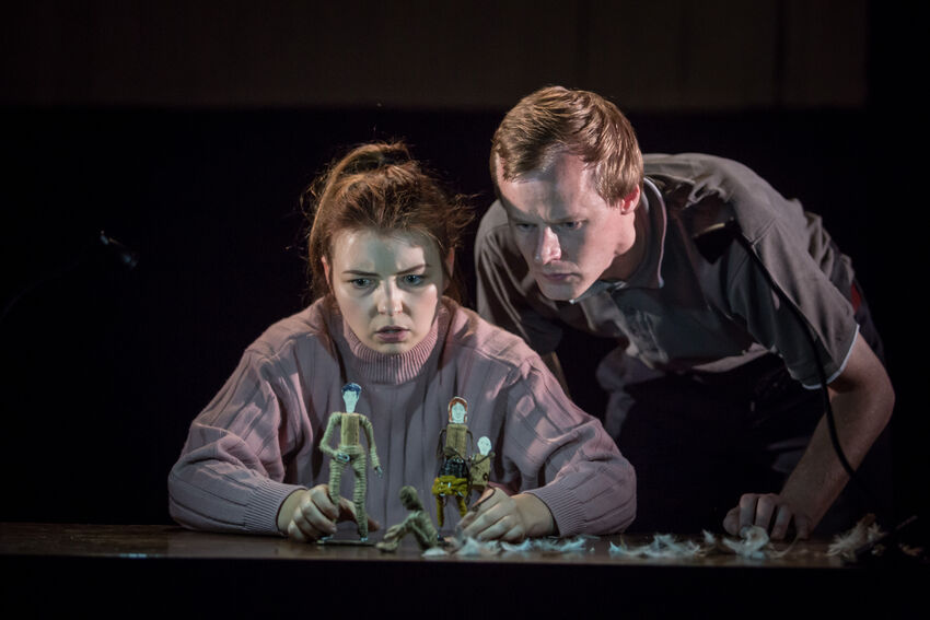 Two performers examine a series of small figurine puppets on a table