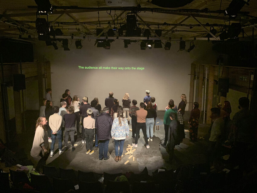 A group of people stand on stage looking at a projection on a screen