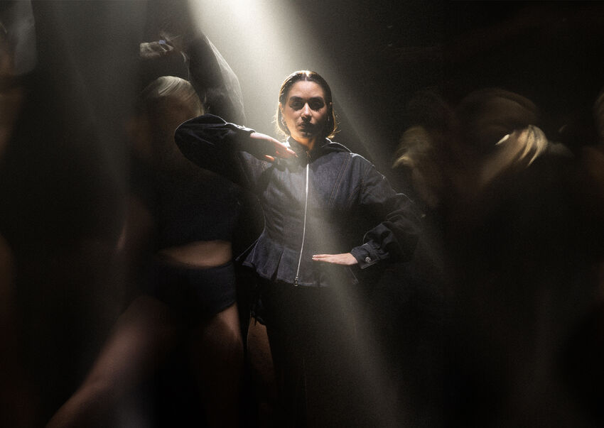 A dancer wearing all black strikes a powerful move, staring straight at the camera