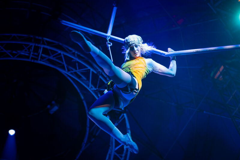 A woman hangs from some poles, kicking her leg out and looking downward