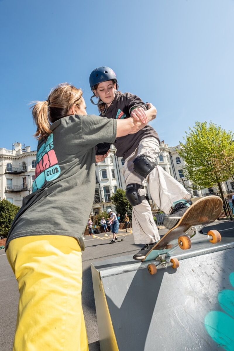 A young girl skateboarding whilst a tutor guides her