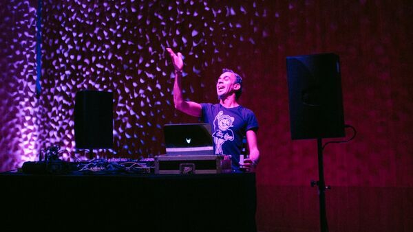 Nerm at a DJ booth with his hand in the air, purple and red lights surround him