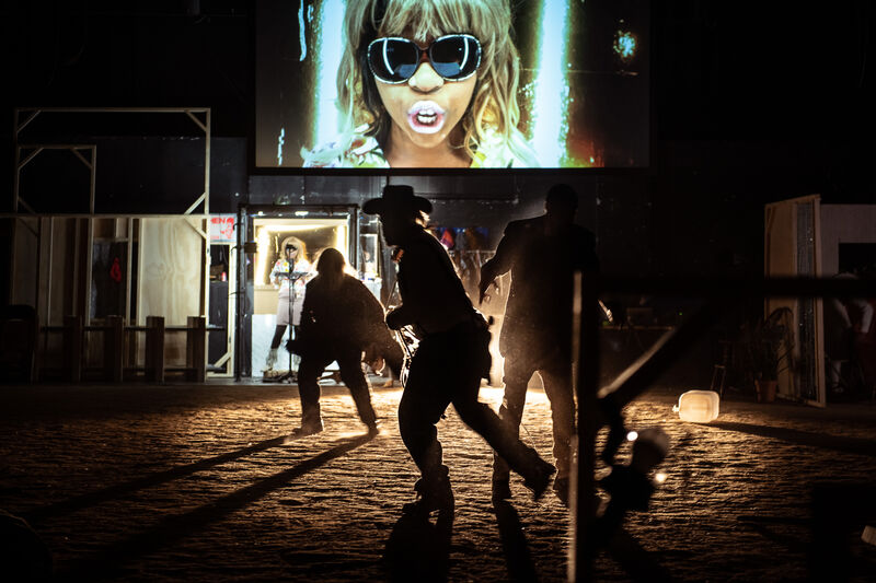 People dressed as cowboys run around in darkness with a light illuminating their figures from behind