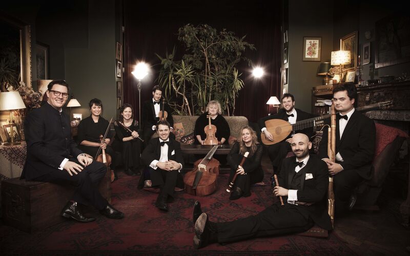 La Nuova Musica sitting around a room on chairs and the floor, holding their instruments