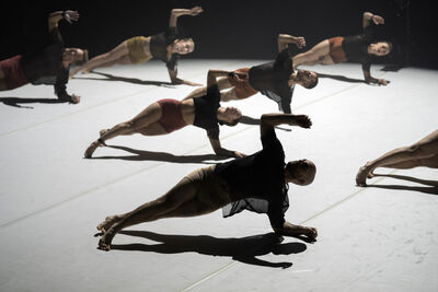 6 people lying on one arm on a dim stage