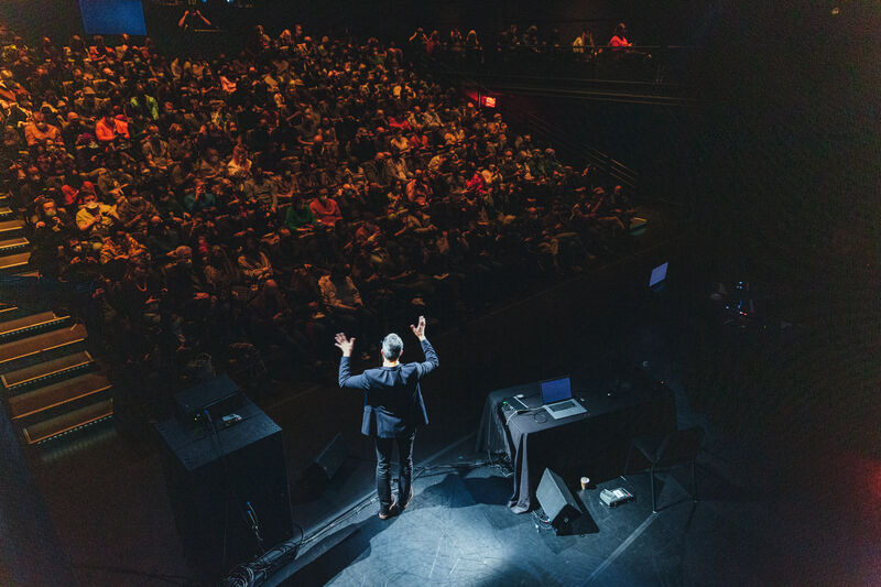 A photo from the back of a stage of a man in a suit talking animatedly at the audience