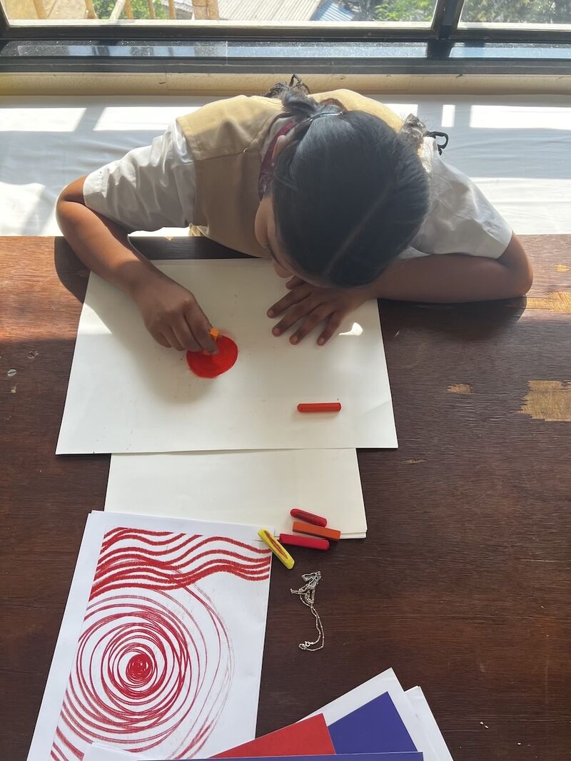 A girl sits at a table drawing a red circle on a white sheet of paper