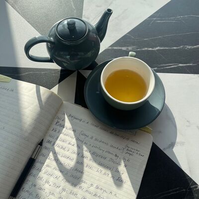 Bird's eye view of a table with a teapot, a cup of tea, a notebook and a pen