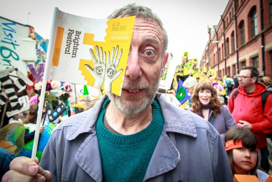 A photo of Michale Rosen at the Brighton Festival children's parade, holding a promotional flag in front of his face