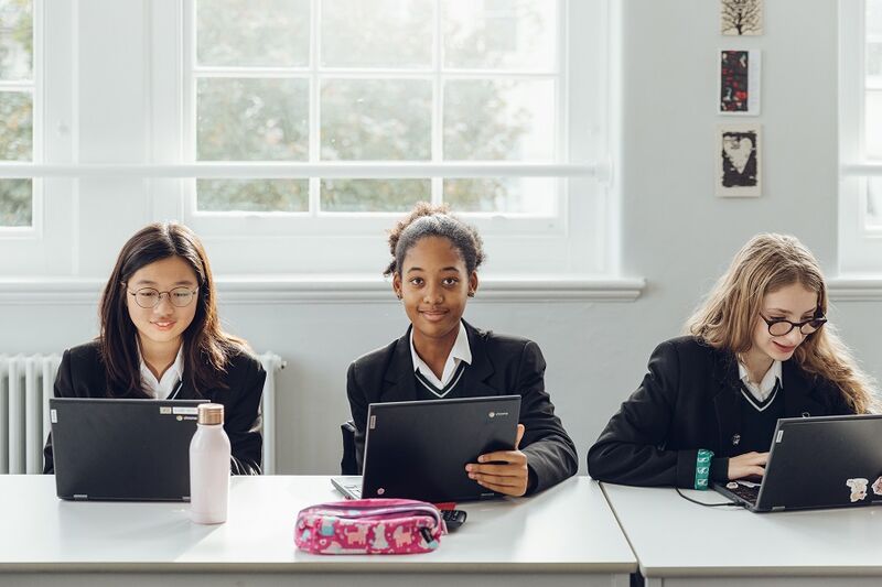 Three students sitting at a desk, all on laptops