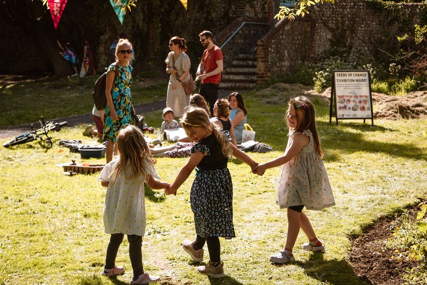 Three young girls holding hands whilst standing in a grassy park
