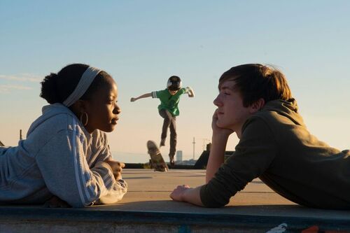 Young actors playing Romeo and Juliet lay on a skate park floor, leaning on their arms and staring at each other.