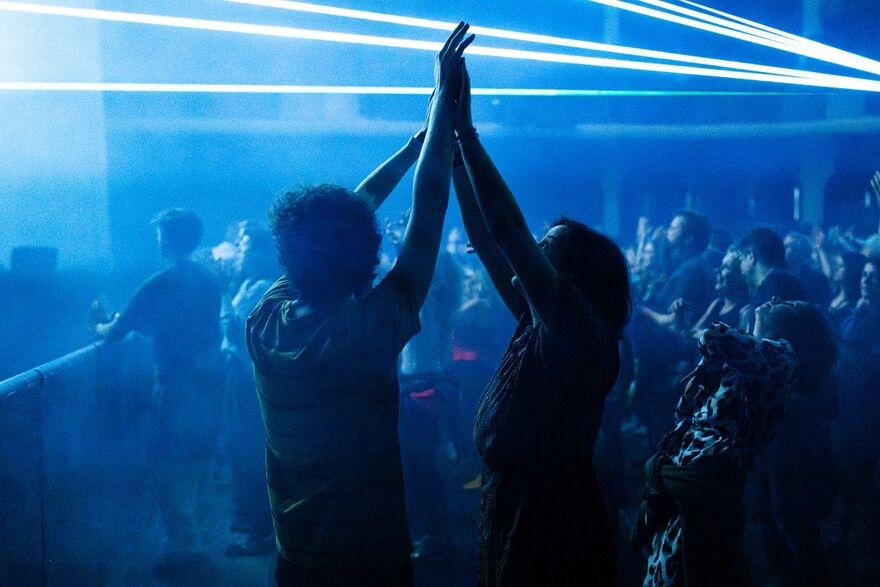 Two people with their hands raised up, touching, beneath beams of lasers
