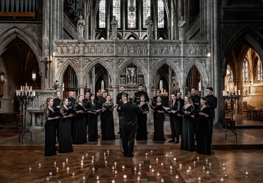 Tenebrae choir standing in all black in a church, they are surrounded by candles