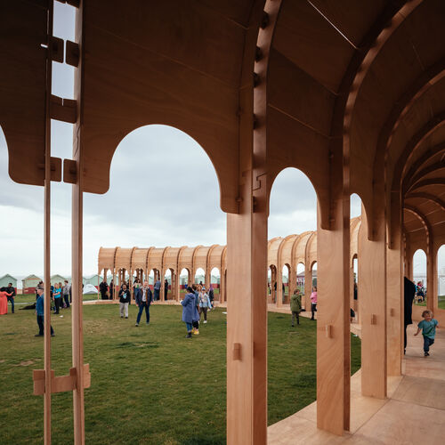 People stand on grass outside The Riwaq and children run along the structure inside