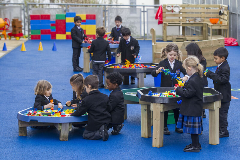 A group of young school children playing in an exciting classroom with blue carpet and activity tables