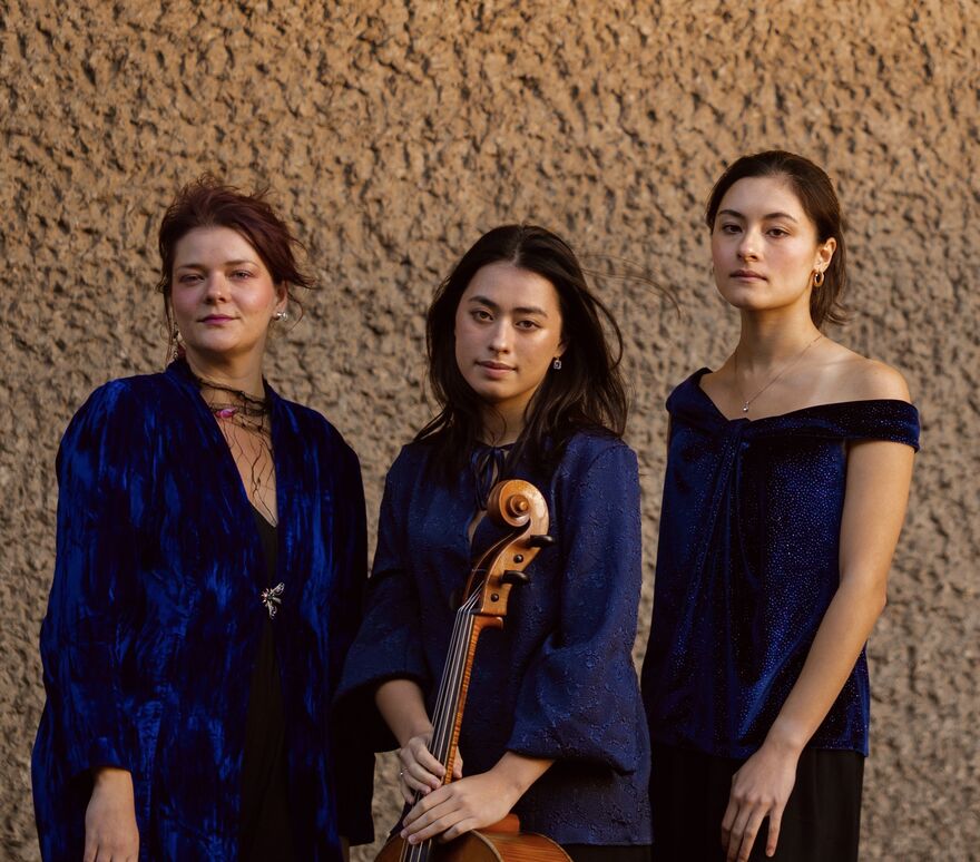 Astatine Trio standing in blue dresses at dusk.