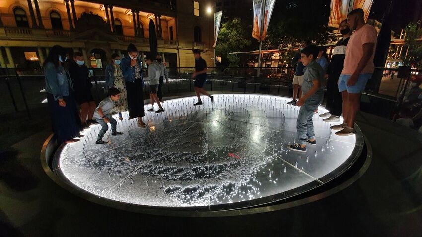 Two groups of people walk on Groundswell which is lit from beneath