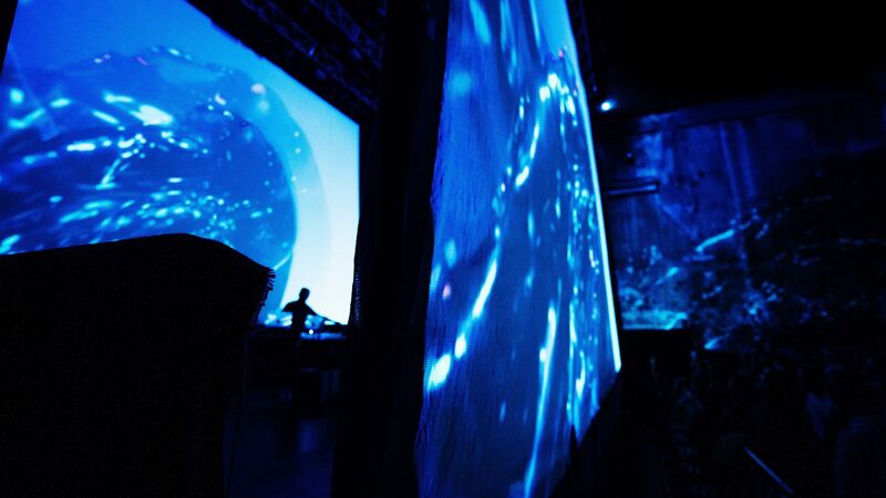 Two screens with blue projections, Max Cooper DJs between them