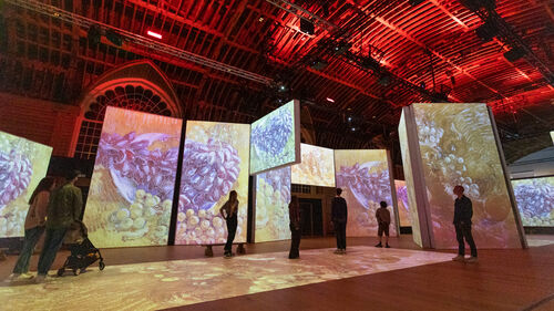The Van Gogh Alive exhibition shows one of the artist's still life paintings, projected onto screens. It is displayed in the Corn Exchange, which is uplit with red lighting.