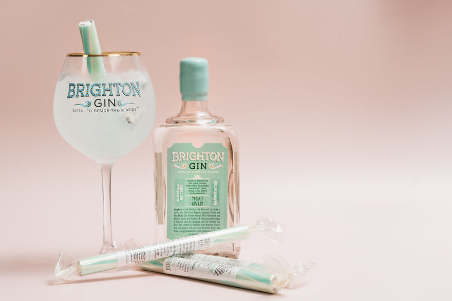 A bottle of Brighton Gin stands next to a goblet of gin and tonic and some sticks of rock