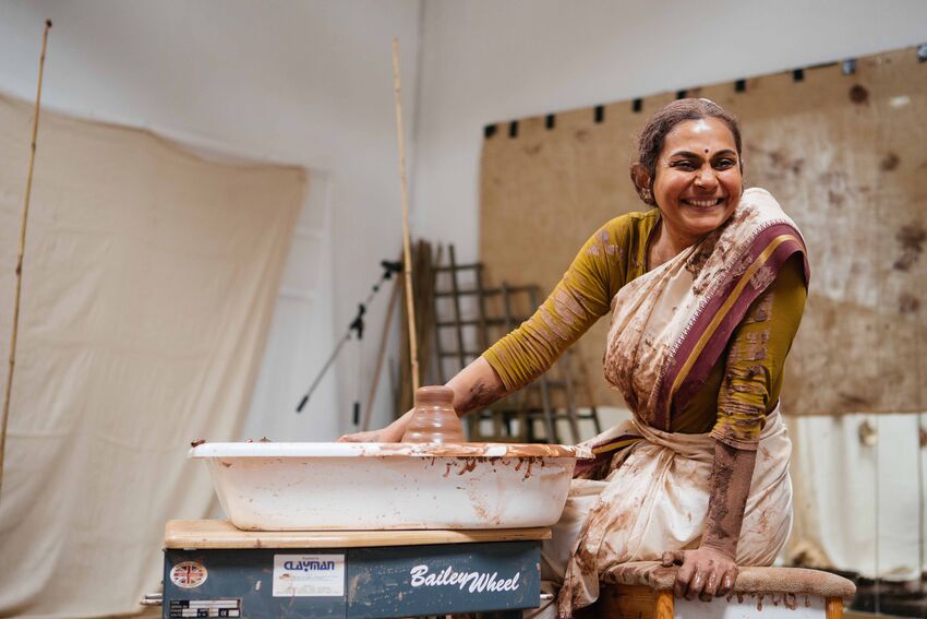 A person wearing a sari smiles whilst moulding clay