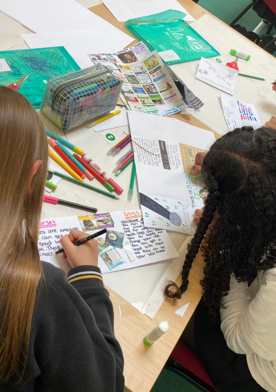 Two girls creating a magazine with felt tip pens and pictures