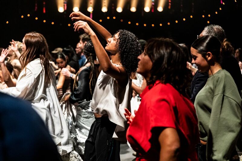 People dancing, with a focus on someone in the middle raising their arms and looking relaxed