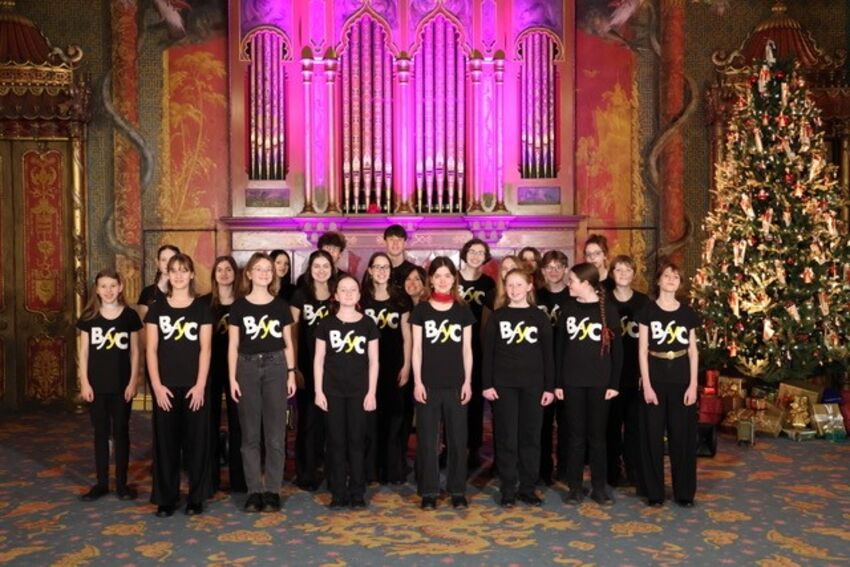 A youth choir standing in front of a grand organ that is lit up purple