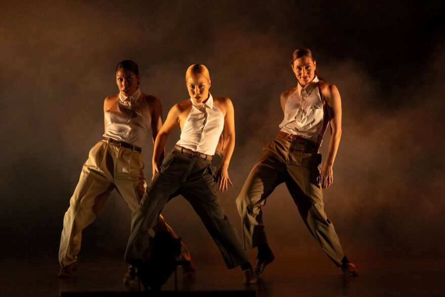 The 3 female dancers in Femme Fatale in a triangle formation, wearing formal trousers and a shirt without the sleeves