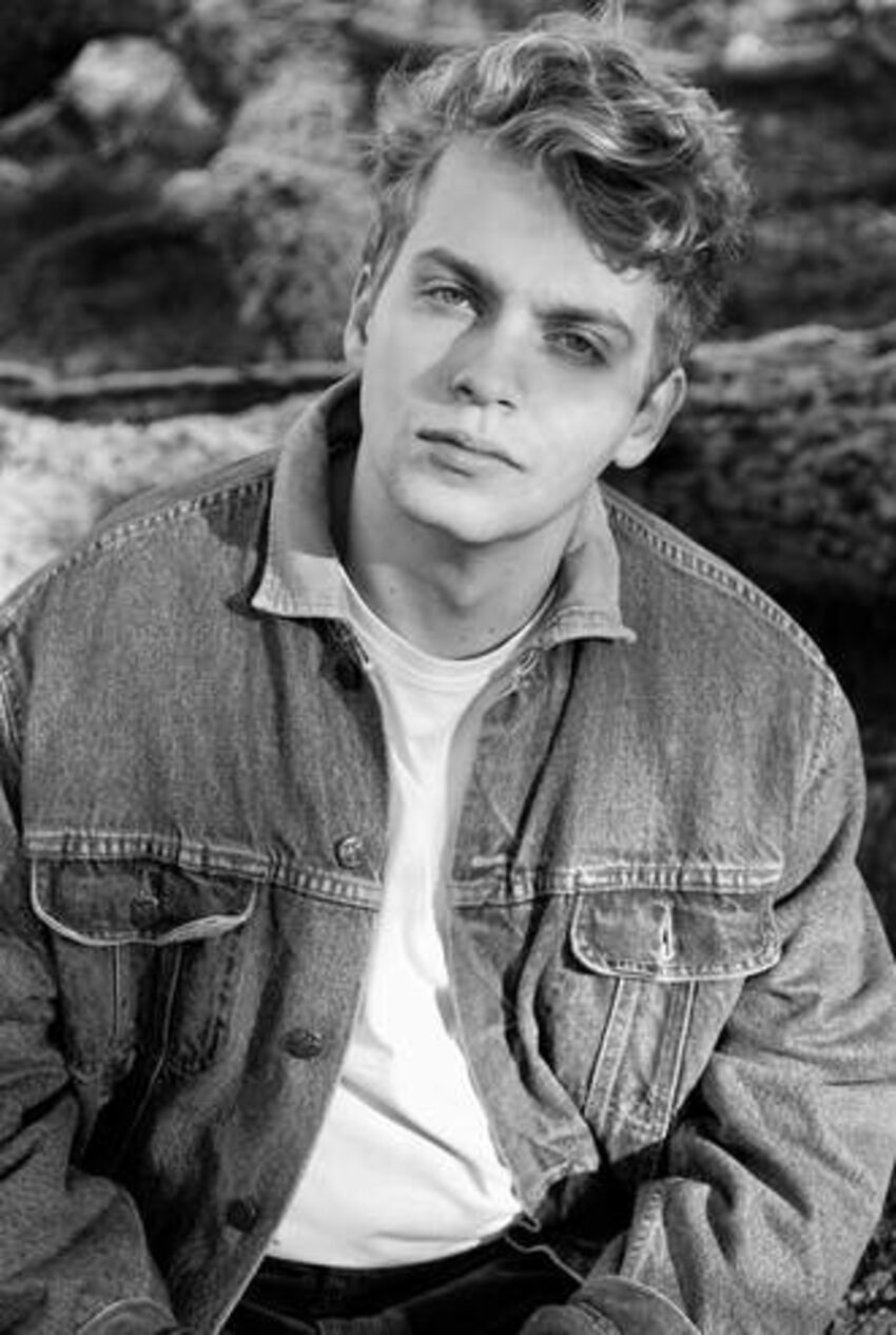  black and white photo of Hugh Cutting, with short blond wavy hair, wearing a white t-shirt and denim jacket