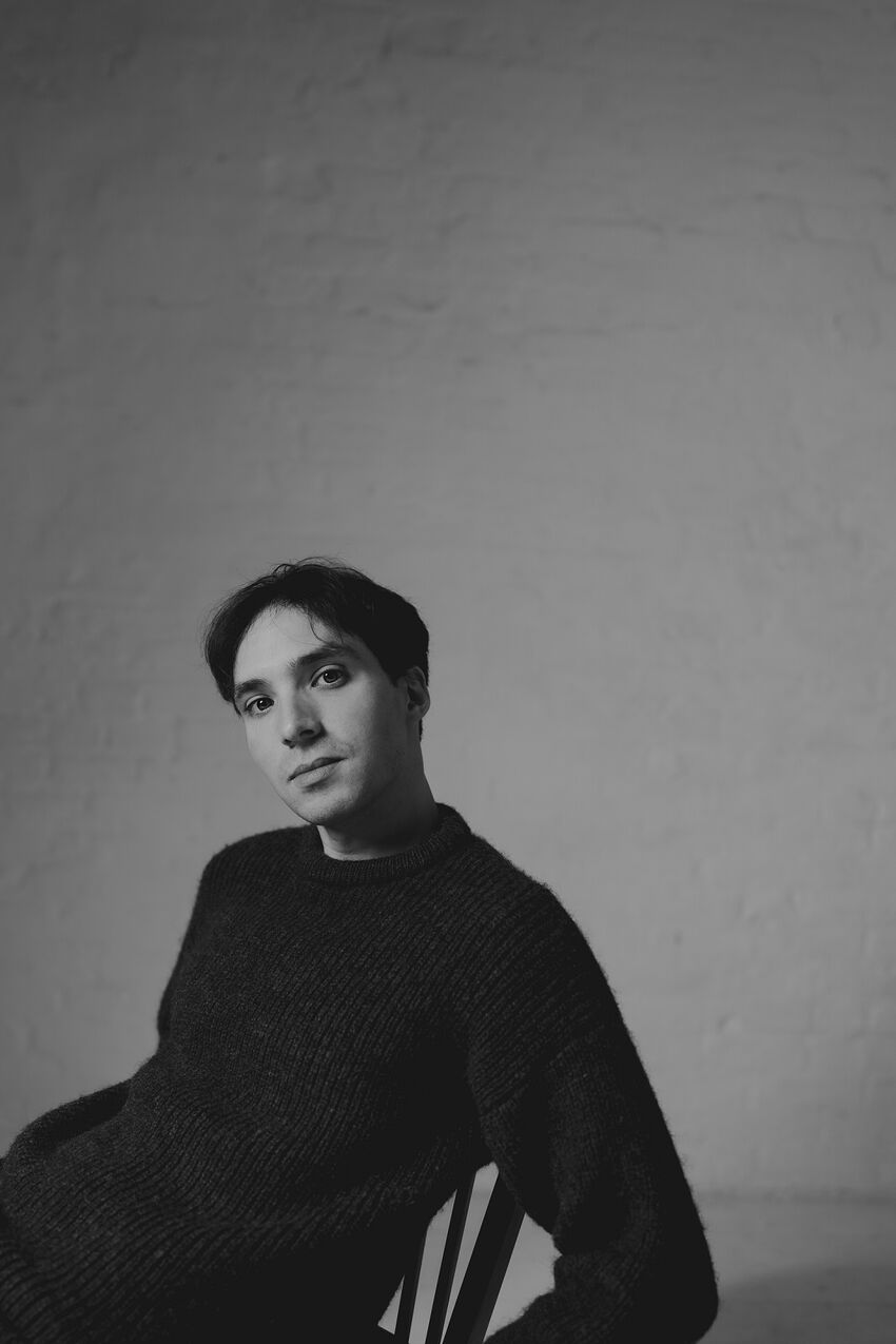 Jonathan, a white man with short black hair, sits casually in a wooden chair